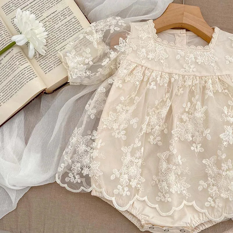 Newborn baby girl's short-sleeve white cotton bodysuit with lace trim and floral embroidery.