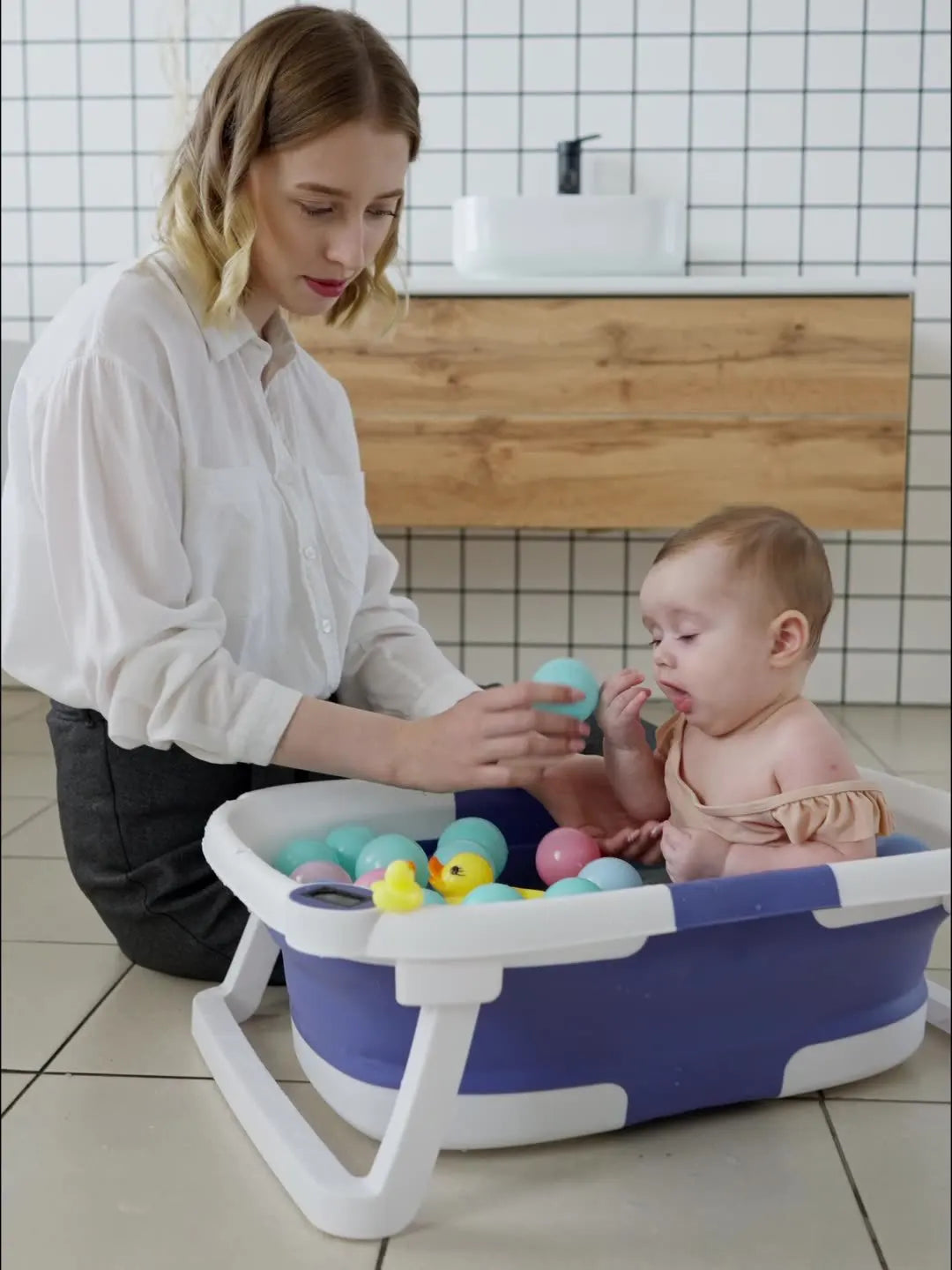 Lifestyle image: Foldable baby bathtub stored upright in a small bathroom, saving space