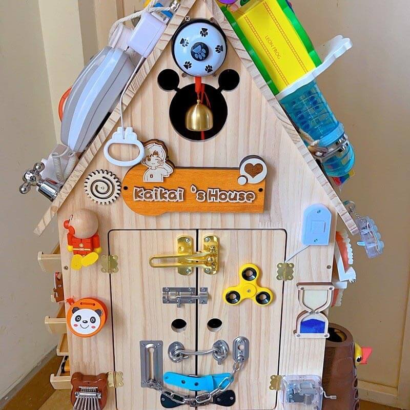 Smiling toddler engaged with a wooden sensory busy house toy, demonstrating early learning and fun.