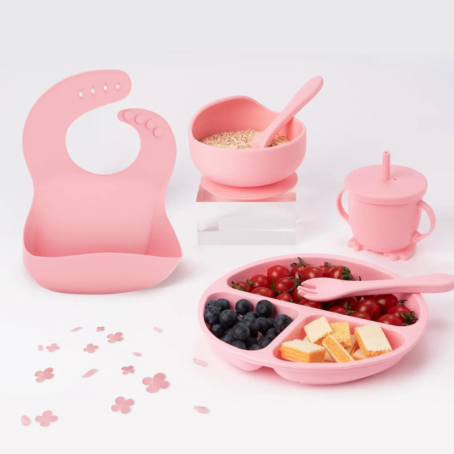 6-piece children's silicone feeding set in muted green, including bib, plate, bowl, cup, spoon, and fork.