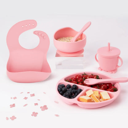6-piece children's silicone feeding set in muted green, including bib, plate, bowl, cup, spoon, and fork.