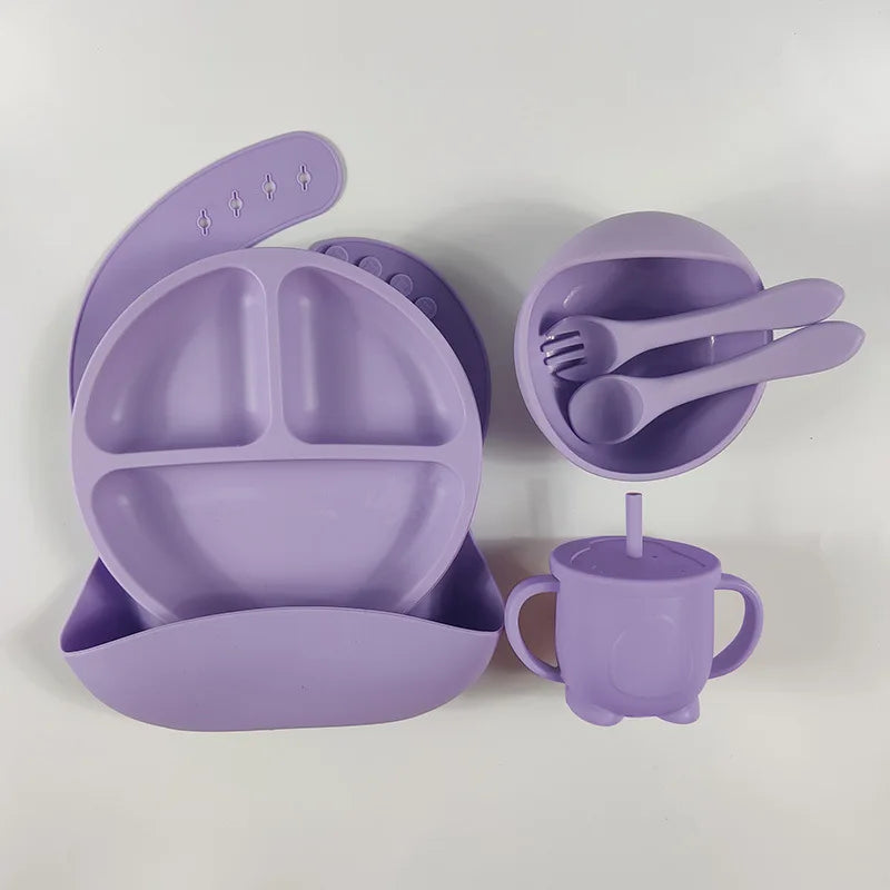 Eco-friendly silicone feeding kit for kids, containing a bib, plate, bowl, cup, spoon, and fork in a single color.