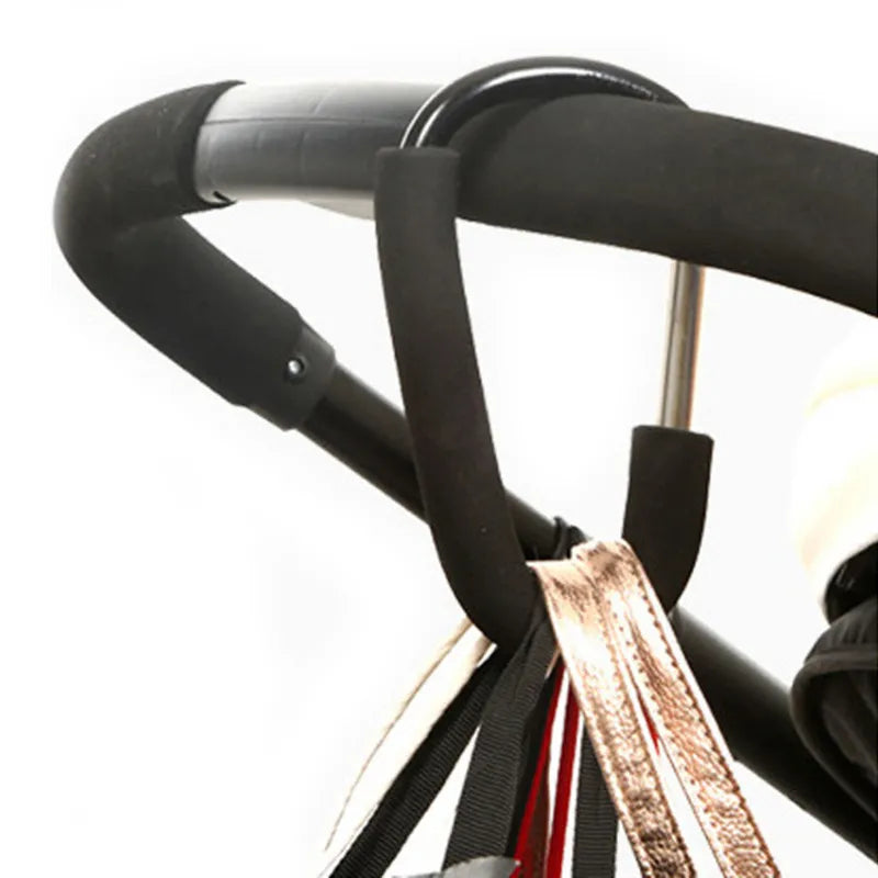 A pair of black heavy-duty stroller hooks organizing bags on a baby stroller handle, perfect for hands-free parenting.