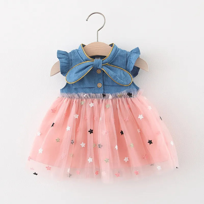 Full shot of a toddler girl wearing a stylish denim dress with a bow and flying sleeves.