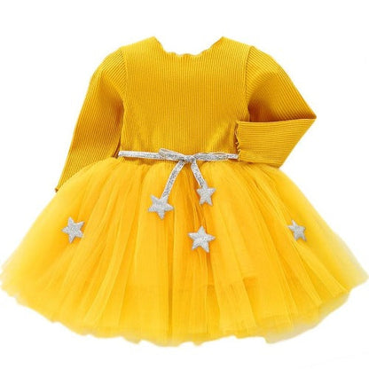 Toddler girl smiling in a festive long sleeve mesh star dress, ideal for holiday or birthday parties.