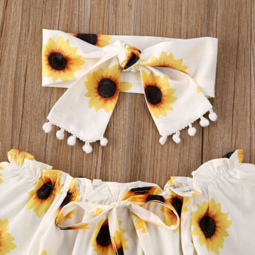 Smiling baby girl wearing a vibrant sunflower print romper and coordinating bow headband. Perfect summer outfit.