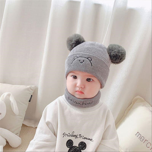 Adorable baby in a cozy white knit hat and matching scarf, perfect for winter warmth.