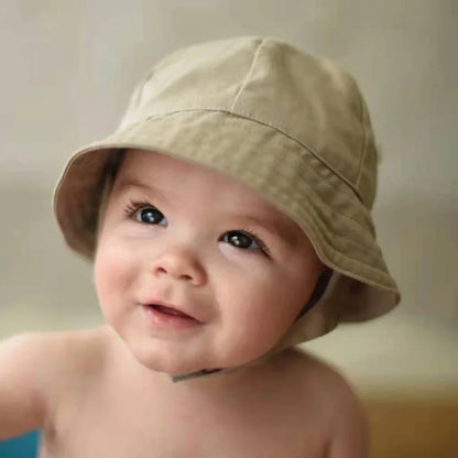 Toddler wearing blue adjustable sun protection bucket hat, exploring a sunny beach, side view.
