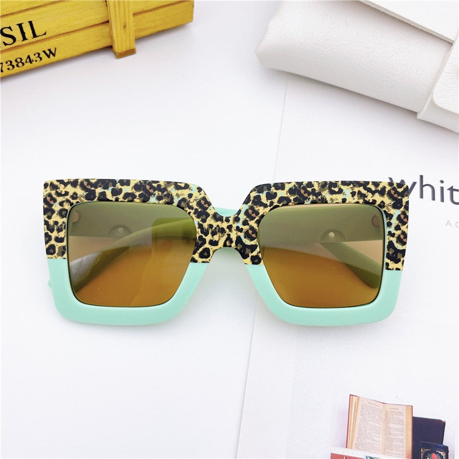 Leopard print baby sunglasses on a beach towel, suggesting use for sun protection during outdoor play.