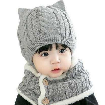 Full view of a baby modeling a warm knitted cat hat and scarf set, great for winter outdoor play.