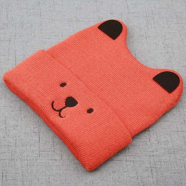 Hand holding a soft knitted bear cub hat, ready for a baby or toddler to wear and stay warm.