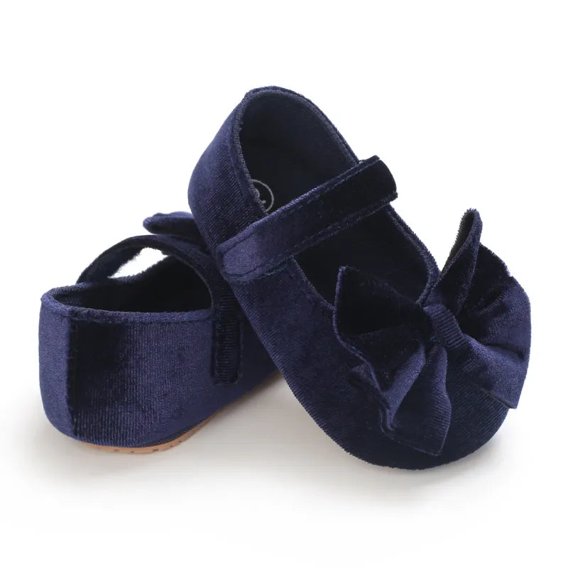 Top view of a pair of white baby girl flat shoes with bows, soft sole, essential first walkers
