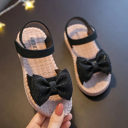 Pair of green girls' bow sandals on a sandy beach, ready for summer fun