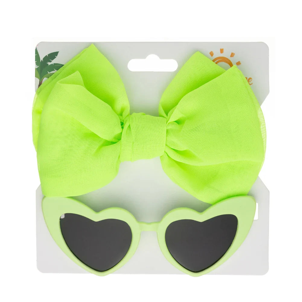 Toddler girl wearing pink heart sunglasses & a bow headband, illustrating cute accessories & baby fashion.