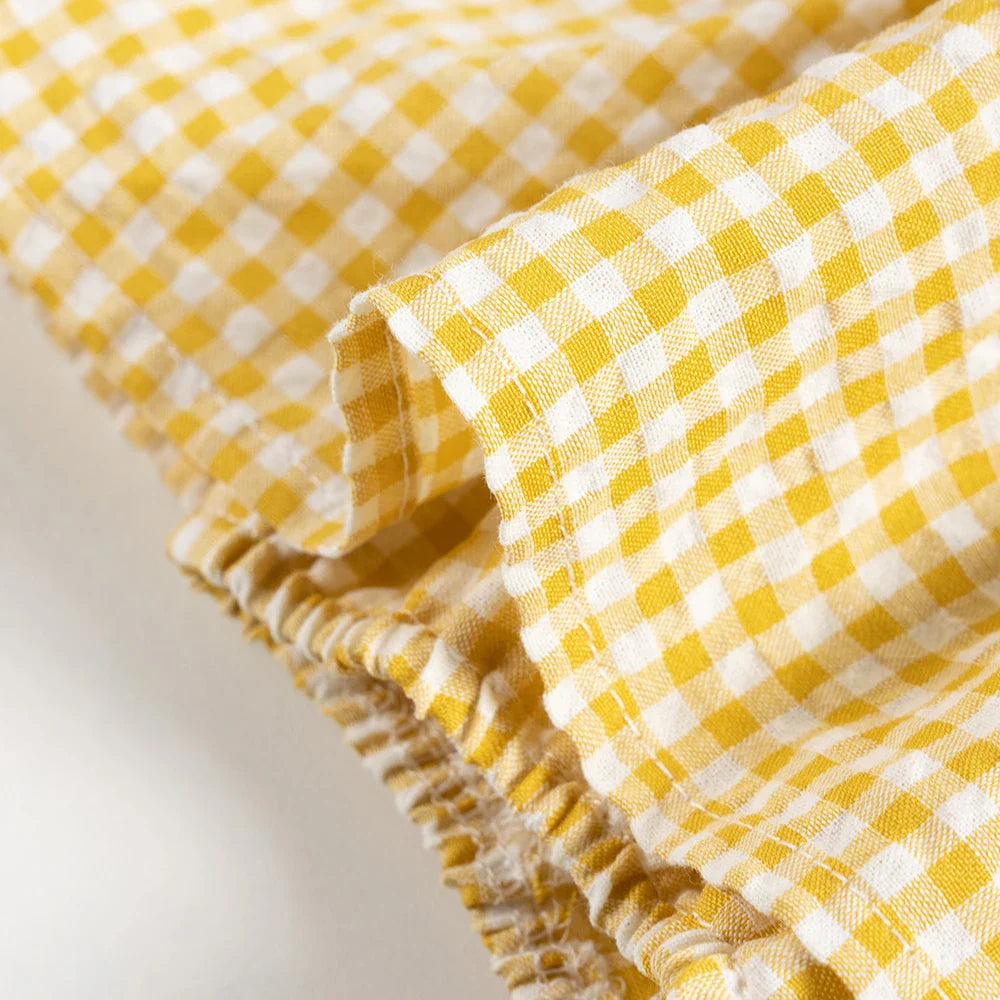 Close-up of the plaid pattern on a girls' cotton romper dress, highlighting fabric detail
