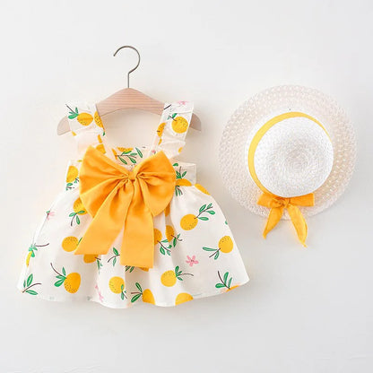 Toddler girl in a vibrant fruit print summer dress & woven straw hat, ideal for beach or park outfits