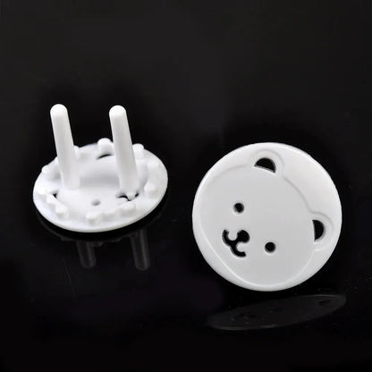 Hand demonstrating installation of a white bear socket cover onto an electrical outlet for child safety.