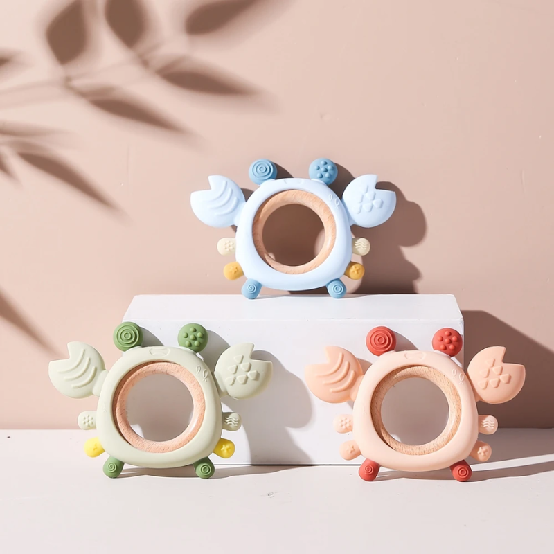Baby biting blue silicone crab teether with wooden ring for gum relief, on white background