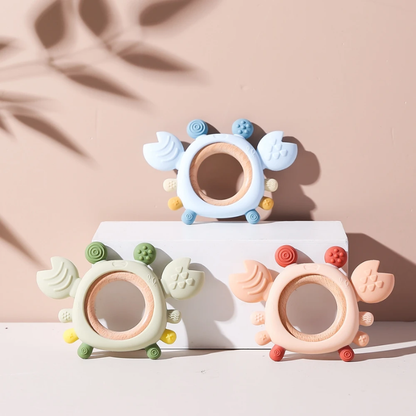 Baby biting blue silicone crab teether with wooden ring for gum relief, on white background