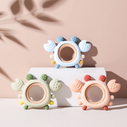Baby biting blue silicone crab teether with wooden ring for gum relief, on white background