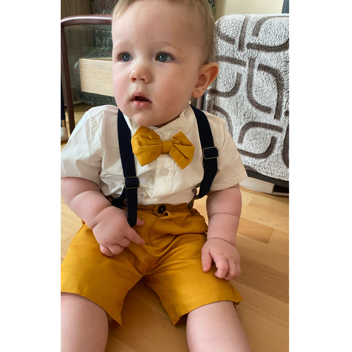 Close-up of baby boy tuxedo set featuring a crisp white cotton shirt, black bow tie, and adjustable suspenders