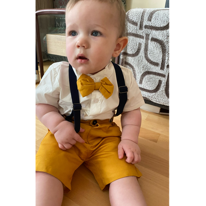 Close-up of baby boy tuxedo set featuring a crisp white cotton shirt, black bow tie, and adjustable suspenders