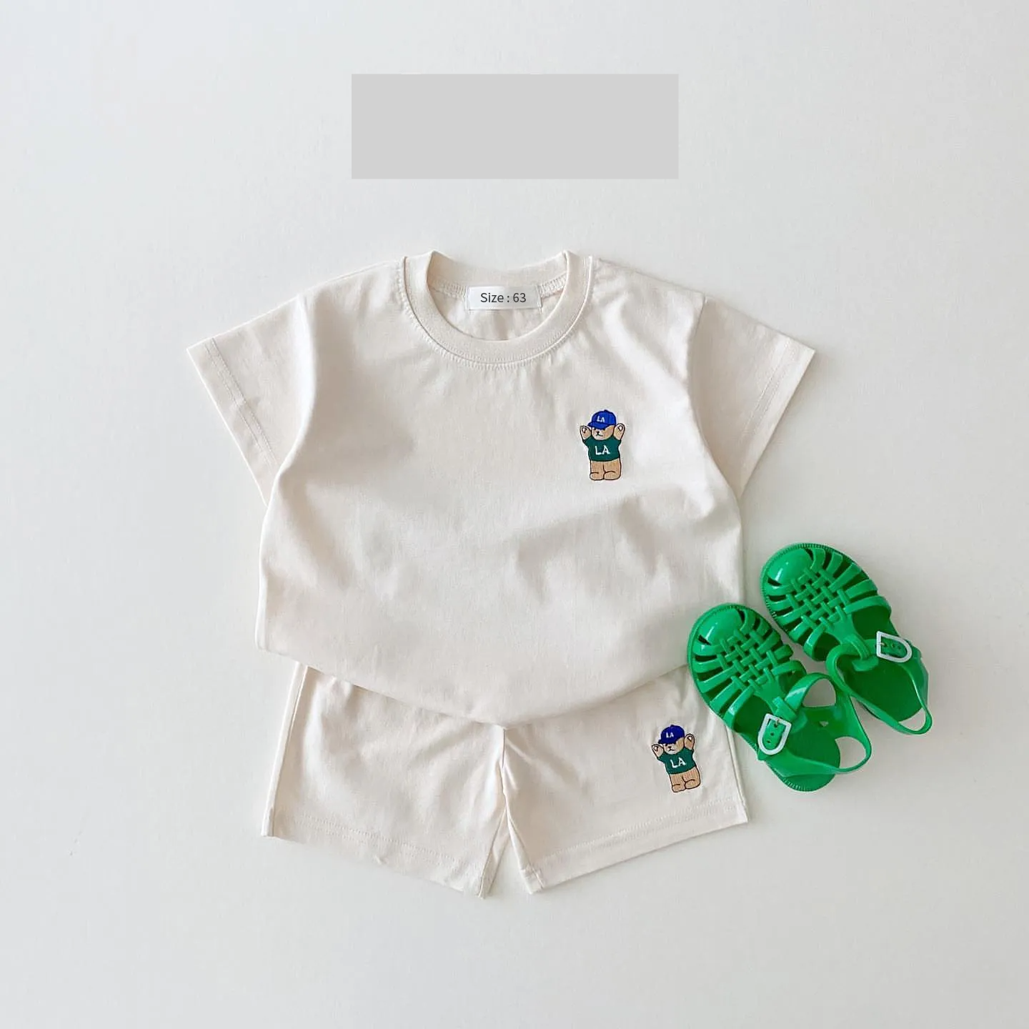 Flat lay of a baby boy's blue t-shirt with embroidered bear and matching white shorts, summer ready