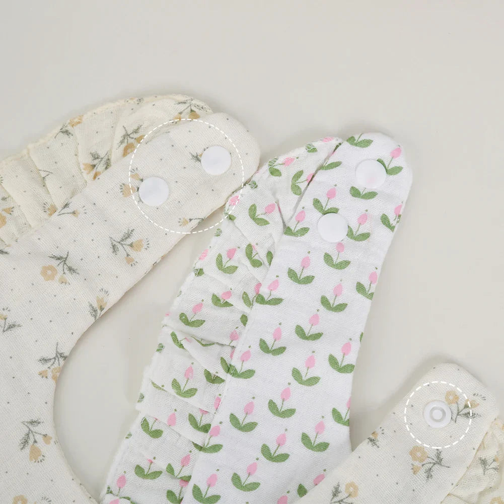 Stack of multiple baby cotton flower print bibs with adjustable snaps, newborn feeding essentials.