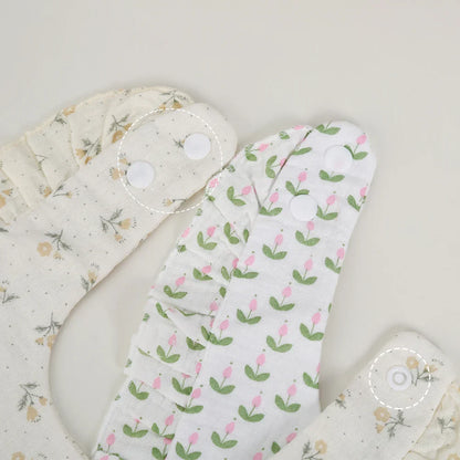 Stack of multiple baby cotton flower print bibs with adjustable snaps, newborn feeding essentials.