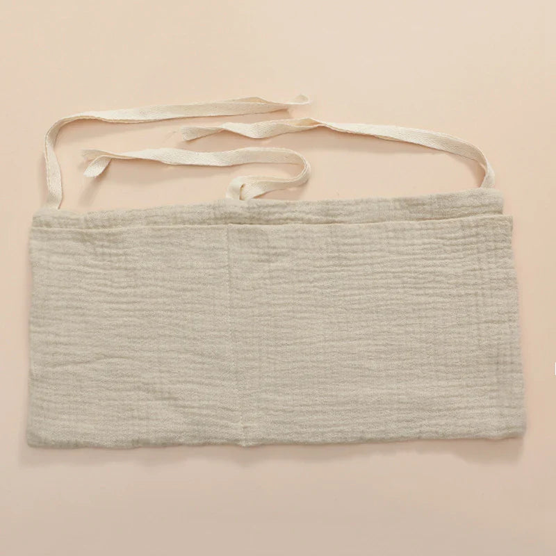 Full view of a baby crib with an attached cotton storage bag, keeping baby items within reach.
