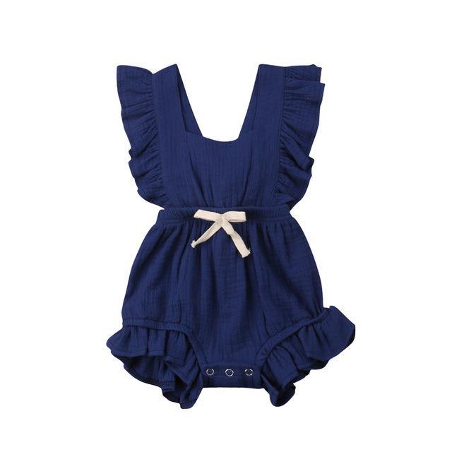 Full shot of a baby girl standing in a ruffled one-piece romper with a charming bow