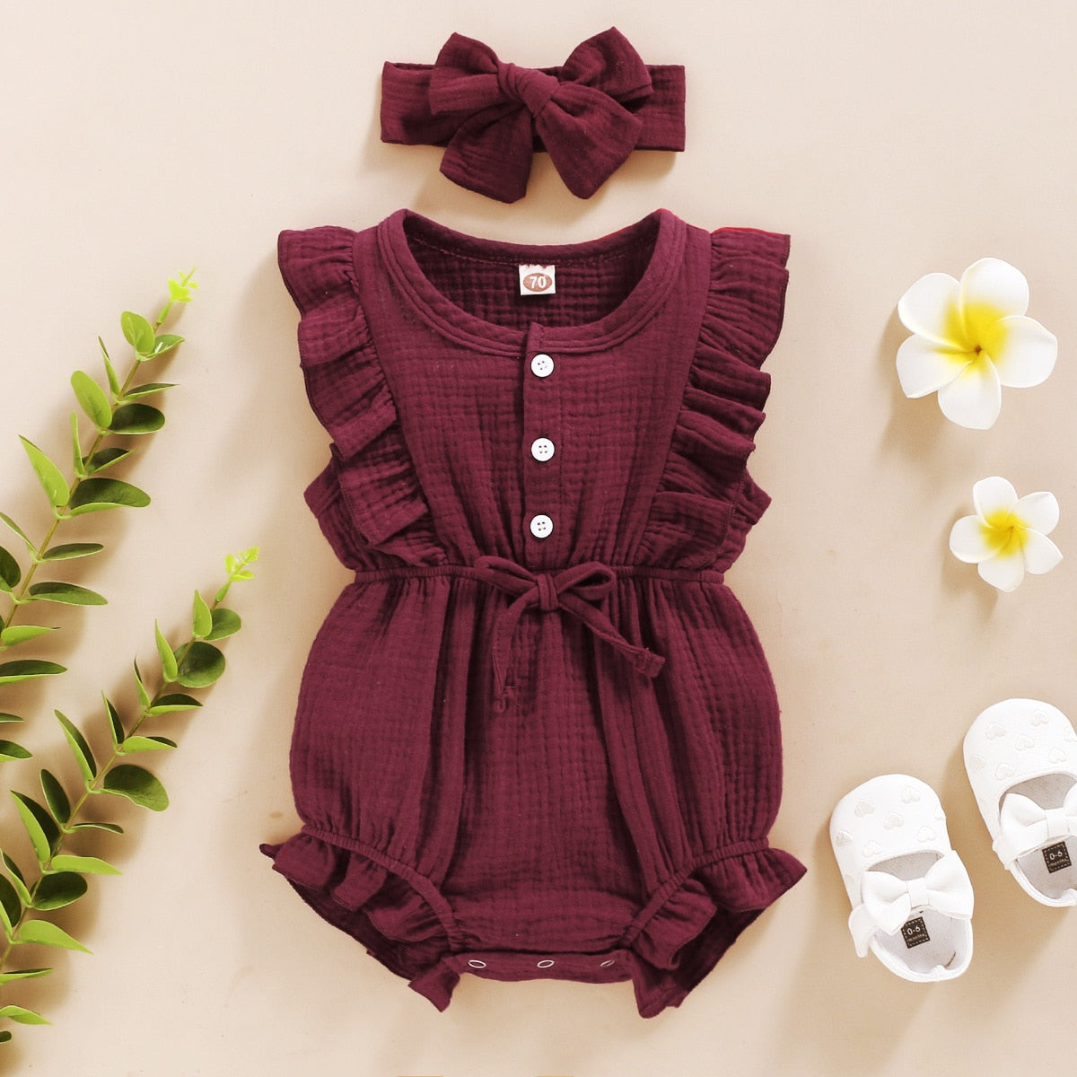 Smiling baby girl on a blanket, wearing a stylish ruffle romper, bowtie, and a decorative headband.