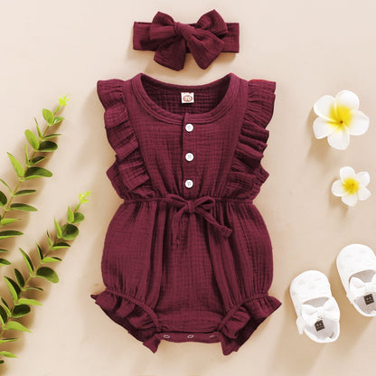 Smiling baby girl on a blanket, wearing a stylish ruffle romper, bowtie, and a decorative headband.