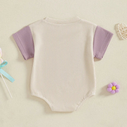 Full-body shot of a baby girl in a purple waffle knit short sleeve jumpsuit, summer romper, casual.