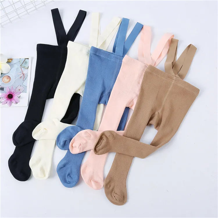 Playful baby girl sitting in striped knit tights with shoulder straps, warm infant legwear.