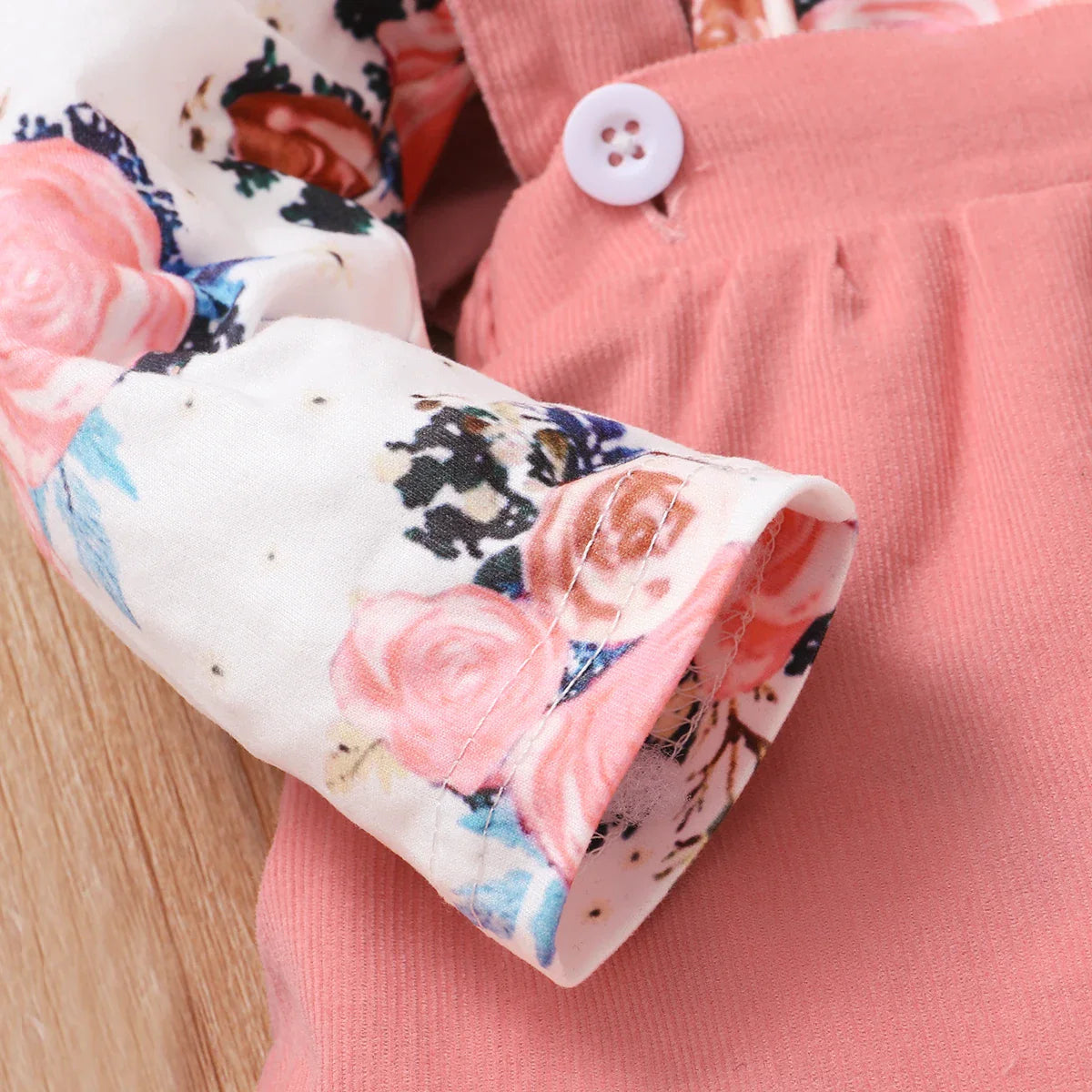 Fashionable baby girl's floral print romper with snap closures, matched with a brown suspender skirt.