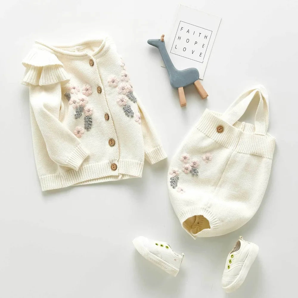 Adorable baby girl in a pink knitted romper & cardigan set, featuring charming flower embroidery. Infant fashion.