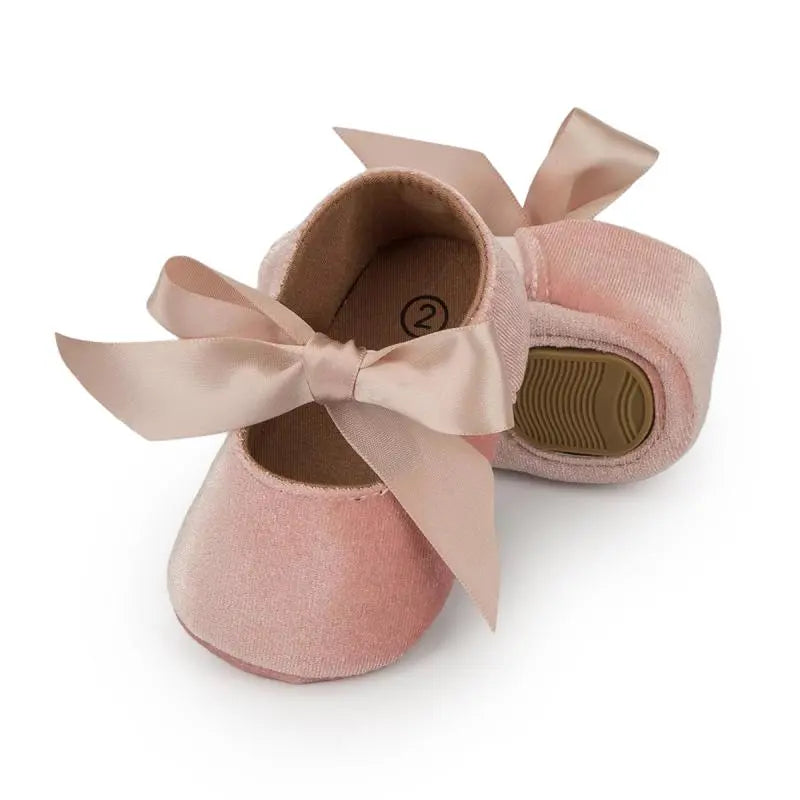 Close-up of a butterfly knot detail on a baby girl's pink soft sole first walker shoe