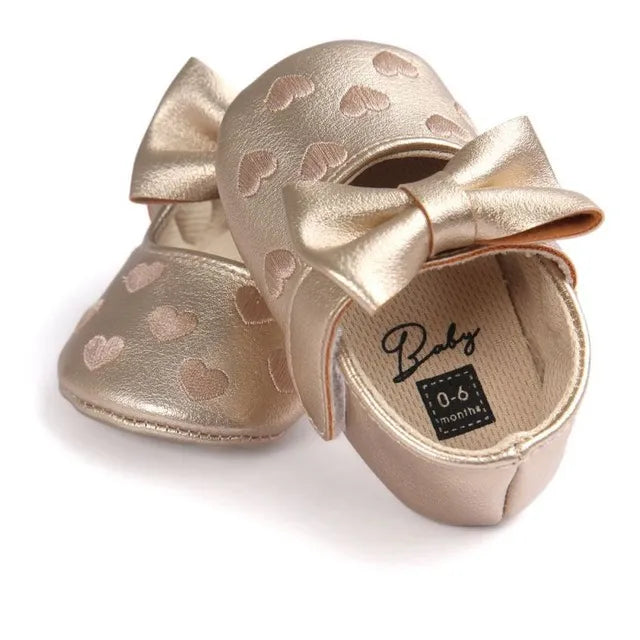 Baby girl moccasins in charming pink, featuring heart pattern and delicate bow fringe