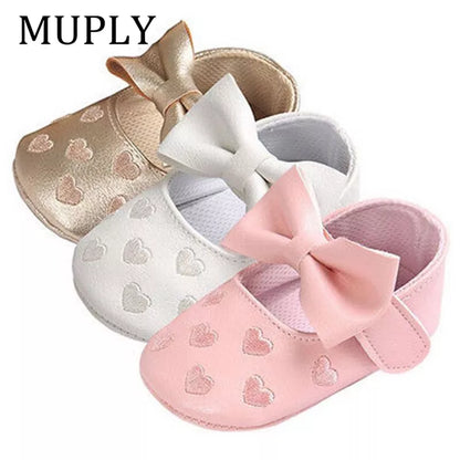 Close-up of pink baby girl moccasins with heart print and bow fringe, soft sole crib shoes