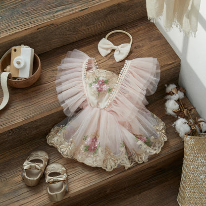 Adorable baby girl wearing a white floral embroidered princess romper and matching headband.