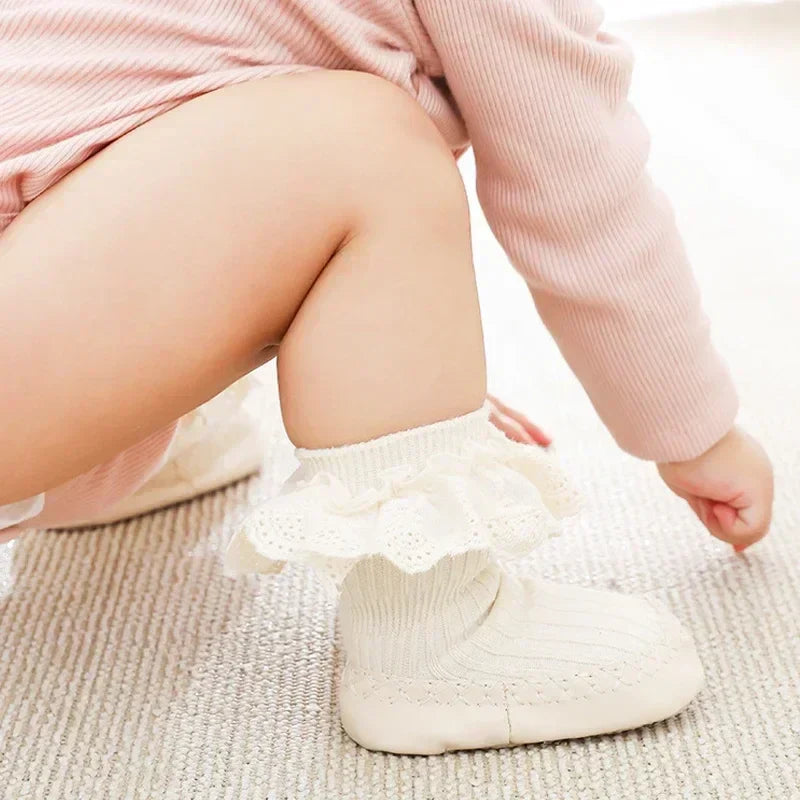 Pair of pink cotton baby girl's sock shoes with anti-slip sole and decorative bow.