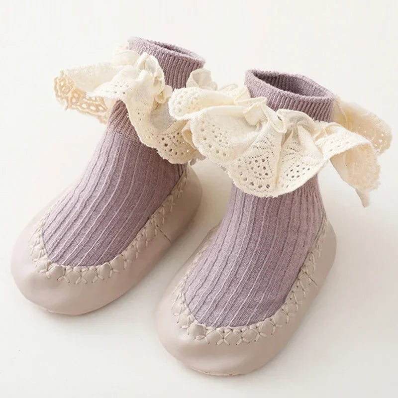 Front view of a single baby girl's anti-slip sock shoe with a pretty ruffle and bow.