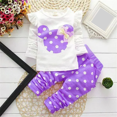 Full view of a baby girl in a pink and white bow dot t-shirt and pants set, ready for play