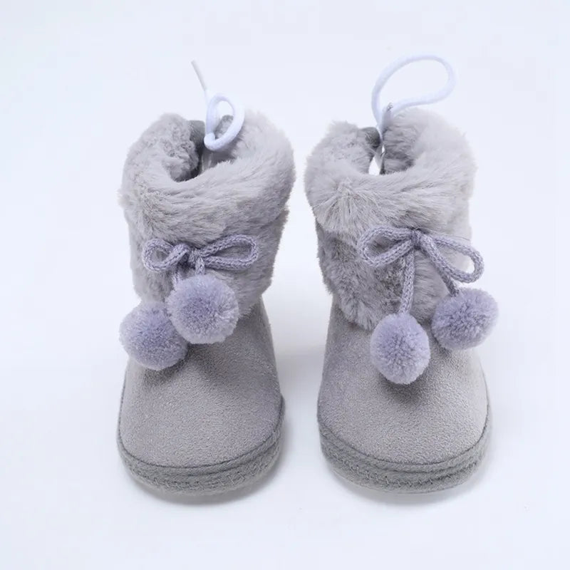 Side view of pink baby girl's winter snow fluff ball bootie, soft sole for infant comfort