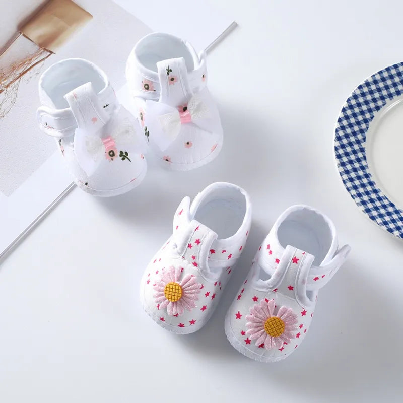 Top view of soft-soled baby girl crib shoes with a vibrant floral pattern and sweet pink bow, spring fashion.