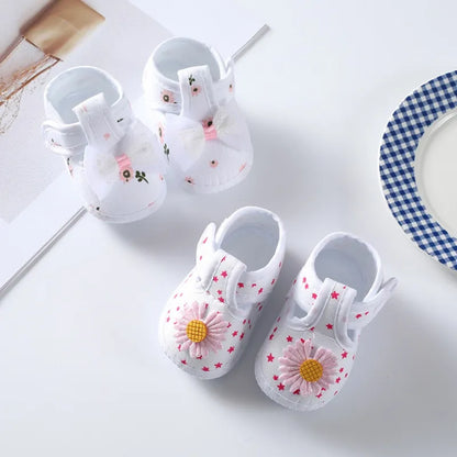 Top view of soft-soled baby girl crib shoes with a vibrant floral pattern and sweet pink bow, spring fashion.