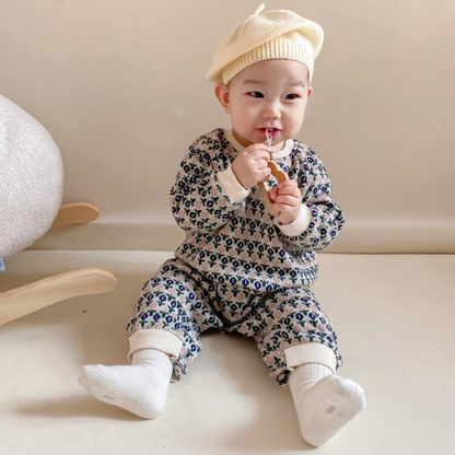 Styled shot of a baby girl wearing a charming floral knitted romper; comfortable fall/winter baby clothes.