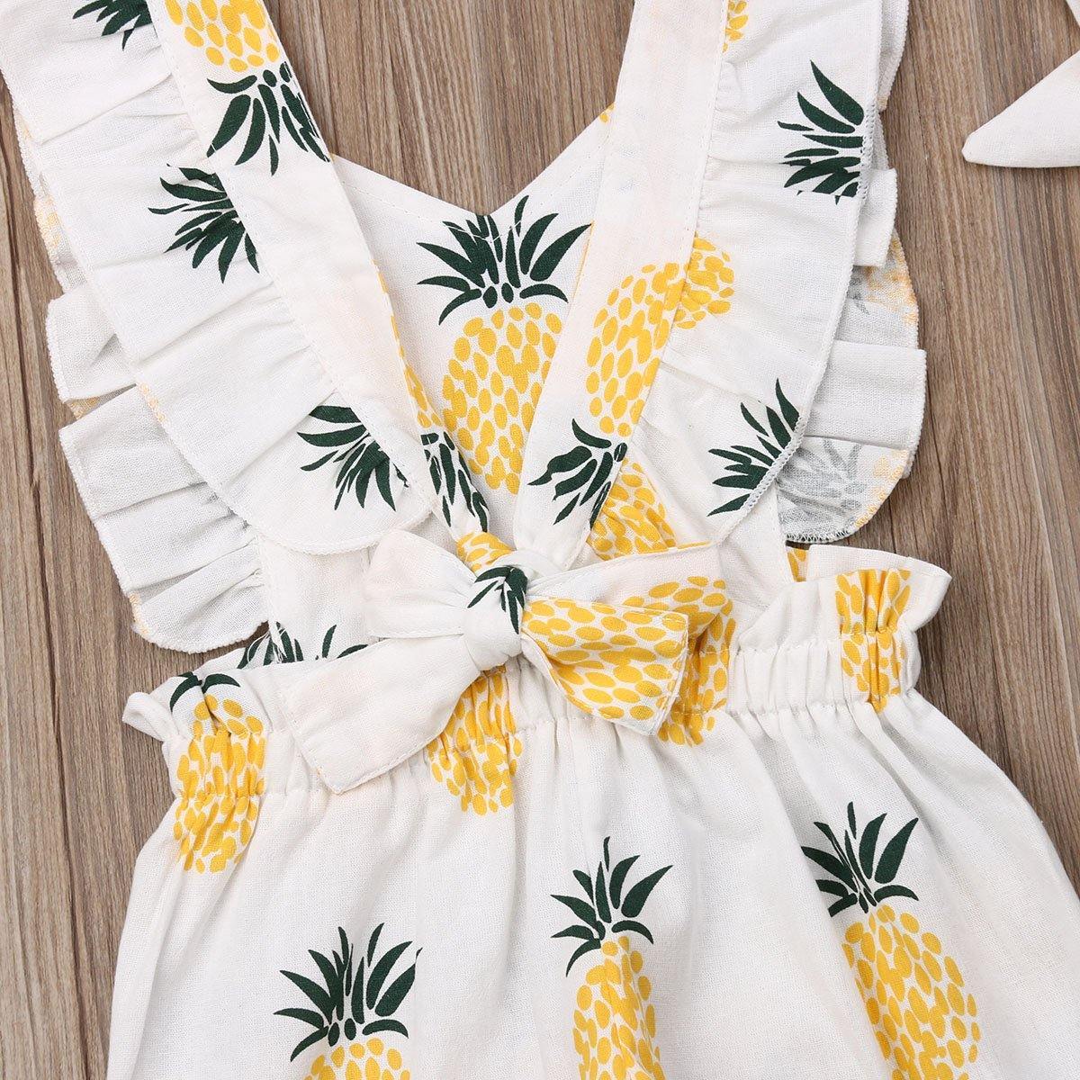 Flat lay of a baby girl's summer romper jumpsuit with a repeating pineapple pattern and coordinating headband