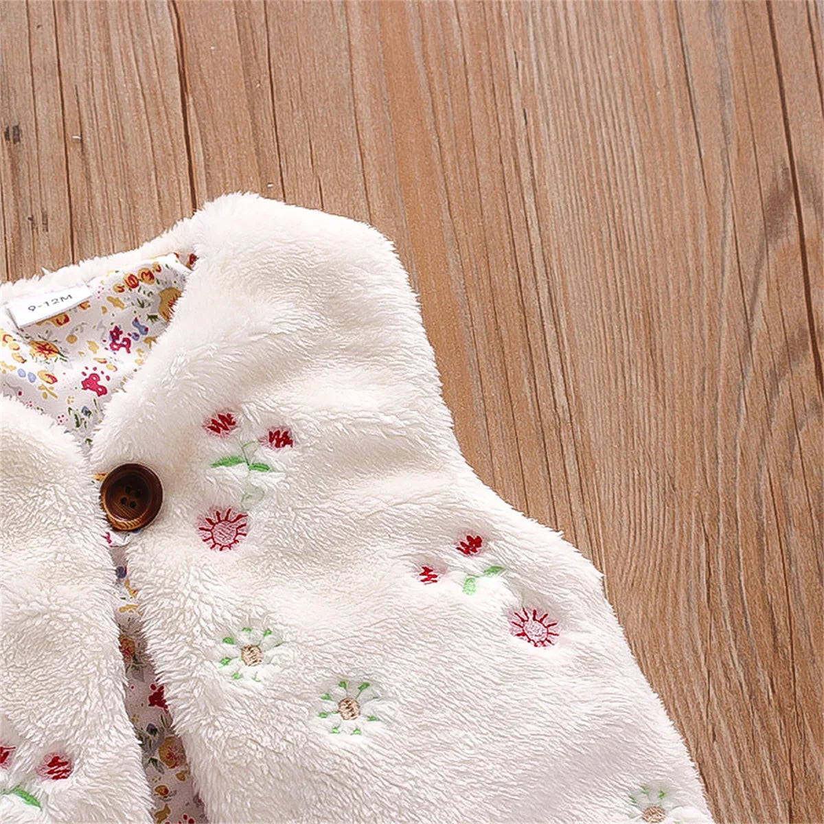 Back view of a baby girl's sleeveless pink fur vest adorned with white flower embroidery.